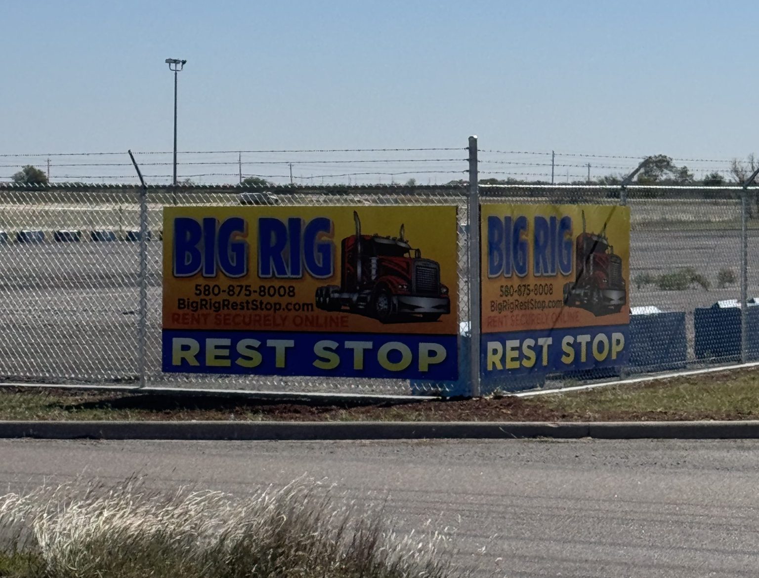 Big Rig Rest Stop signs on the fenced corner of the paved lot